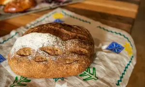 Chleb pieczony w rękawie, z chrupiącą skórką i delikatnym wnętrzem, leży na lnianej serwetce z ludowymi wzorami.