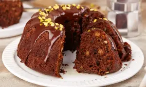 Pyszna babka na oleju, polana czekoladą i posypana pistacjami, z kawałkiem ciasta obok.