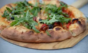 Pyszne ciasto na pizzę z rukolą, oliwkami i papryką, podane na drewnianej desce.