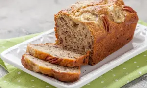 Pyszny chlebek bananowy z orzechami pekan i plasterkami banana na wierzchu, pokrojony na kromki, na białej paterze.