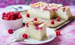 Pyszny sernik z malinami, z kawałkiem na talerzyku i miseczką świeżych malin obok. Idealny deser na letnie popołudnie.