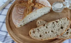 Chleb z mąki żytniej, pokrojony na desce, z solniczką i nożem w tle.