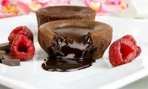 Płynny środek gorącego lava cake spływa na talerz, otoczony malinami i kawałkami czekolady.