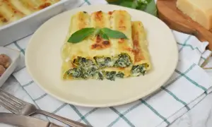 Pyszne cannelloni ze szpinakiem i serem, zapieczone pod beszamelem, ozdobione listkiem bazylii.