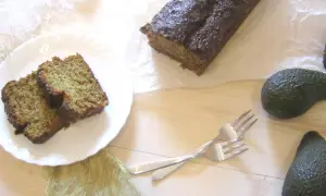 Chleb bananowy z awokado, pokrojony na kromki, leży na talerzu obok całego bochenka. Dwa awokado i widelce dopełniają kompozycję.
