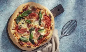 Pyszna pizza bez drożdży z pomidorami i bazylią, podana na drewnianej desce.