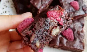 Pyszne brownie z malinami i orzechami, trzymane w dłoni.
