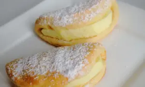 Dwa pyszne ciastka z jabłkami, posypane cukrem pudrem, leżą na białym talerzu.