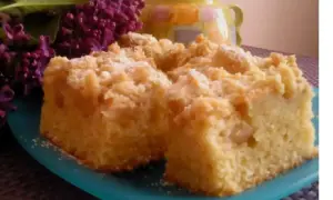 Puszyste ciasto na maślance z kruszonką, podane na turkusowym talerzu, obok bukietu bzu.