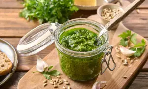 Słoik domowego pesto z pietruszki, obok czosnek, nasiona słonecznika i kawałek chleba.