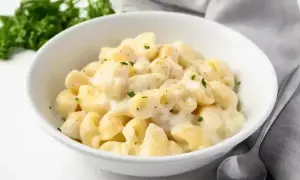 Makaron w kremowym sosie śmietanowym, posypany natką pietruszki, w białej misce. Obok łyżka i serwetka.