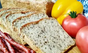 Pyszny chleb nocny na zakwasie, pokrojony w kromki, obok wędzonej kiełbasy, pomidorów i żółtej papryki.