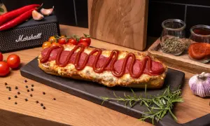 Pyszna zapiekanka z salami, posypana serem i polana ketchupem, prezentuje się apetycznie na desce. Obok czosnek, pomidorki i przyprawy.