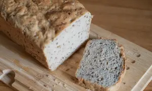 Chleb z siemienia lnianego, z jedną kromką obok, na desce do krojenia.