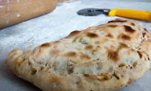 Złocisty calzone, gotowy do podania. Obok wałek i nóż do pizzy, jakby ktoś właśnie skończył przygotowywać ten pyszny przepis.