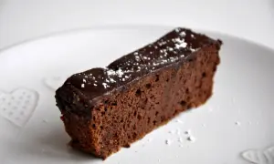Wilgotny brownie z fasoli, polany czekoladą i posypany cukrem pudrem, na białym talerzu z serduszkami.