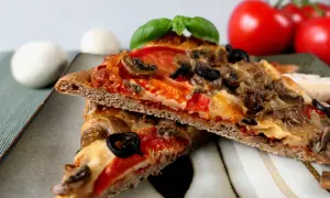 Dwie kromki pizzy na cieście z mąki pełnoziarnistej z pieczarkami, oliwkami i pomidorami.