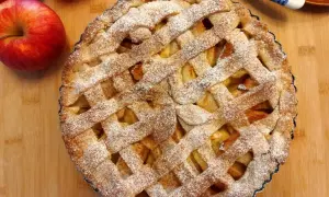 Pyszna tarta z jabłkami, posypana cukrem pudrem, czeka na podanie. Obok leżą świeże jabłka.