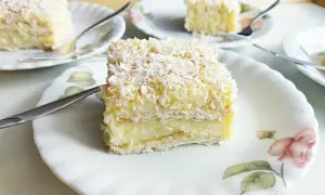 Pyszne ciasto rafaello, warstwowe, z kremem i wiórkami kokosowymi, na talerzyku z różą.