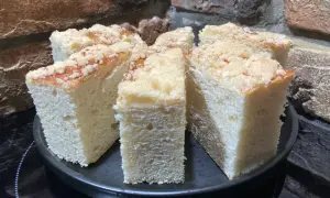 Puszyste ciasto drożdżowe z kruszonką, pokrojone na kawałki, prezentuje się apetycznie na czarnym talerzu.