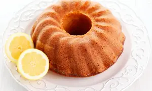 Puszysta babka cytrynowa na ozdobnym talerzu, z dwoma plasterkami cytryny obok. Idealna na popołudniową herbatkę.
