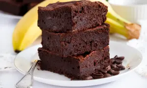 Stos puszystych brownie z bananami, ozdobiony ziarnami kawy, na talerzyku z łyżeczką.
