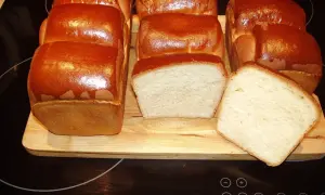 A fresh batch of chleb hokkaido, golden brown and fluffy, awaits. Two loaves are sliced, revealing their soft, airy crumb.