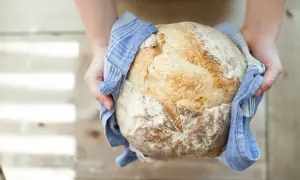 Ręce trzymają okrągły, świeżo upieczony chleb na drożdżach, owinięty w niebieski ręcznik.