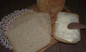 Chleb na zakwasie z maszyny, pokrojony w kromki, jedna posmarowana masłem.