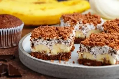 Słodki kopiec kreta z bananami, kremem i czekoladową posypką. Obok babeczka i kawałki czekolady.