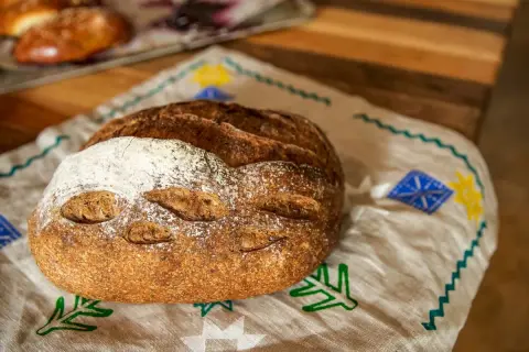 Chleb pieczony w rękawie, z chrupiącą skórką i delikatnym wnętrzem, leży na lnianej serwetce z ludowymi wzorami.