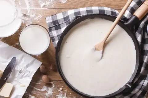 Kremowy beszamel w patelni, obok mleko, masło i gałka muszkatołowa. Idealny przepis na sos.