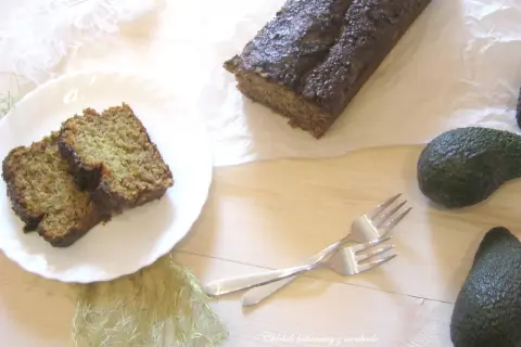 Chleb bananowy z awokado, pokrojony na kromki, leży na talerzu obok całego bochenka. Dwa awokado i widelce dopełniają kompozycję.