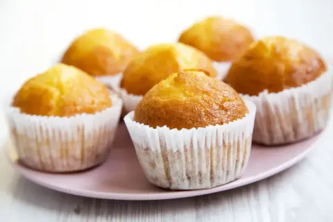 Sześć złotych muffinek w papierowych foremkach na różowej paterze. Idealne na szybki muffinki przepis.