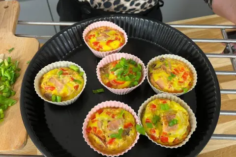 Sześć pysznych muffinek jajecznych z szynką, papryką i szczypiorkiem, gotowych do podania.