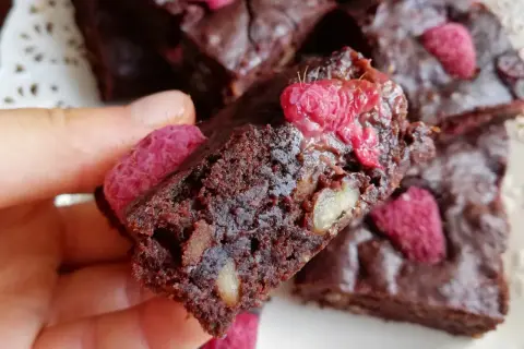 Pyszne brownie z malinami i orzechami, trzymane w dłoni.