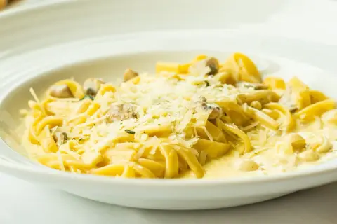 Tagliatelle z grzybami w kremowym sosie, posypane parmezanem. Pyszny sos cebulowy podkreśla smak dania.