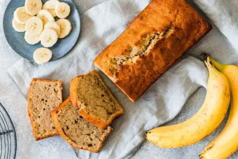 Chlebek bananowy, pokrojony w plastry, z bananami i plasterkami na talerzyku. Kwestia smaku, czy wolisz cały bochenek, czy kawałek.