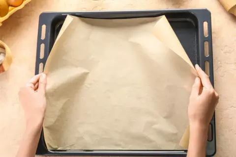Dłonie układają papier do pieczenia na blasze. Zastanawiasz się, czym zastąpić papier do pieczenia? Oto praktyczne rozwiązanie!