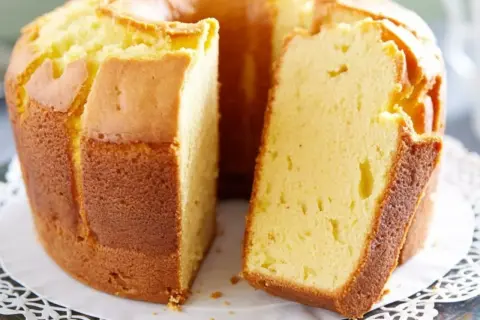 Puszysta babka pomarańczowa, zrumieniona na zewnątrz, z widocznym kawałkiem ciasta. Idealna na popołudniową herbatę.