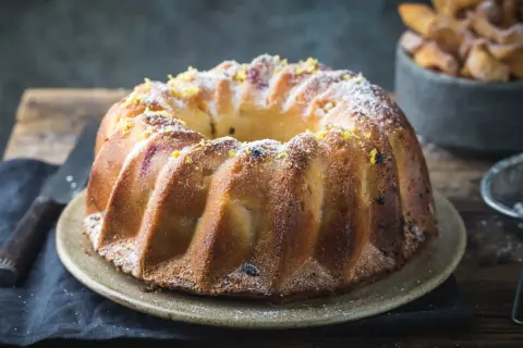 Złocista babka piaskowa, oprószona cukrem pudrem i skórką cytrynową, czeka na talerzu, by umilić popołudnie.