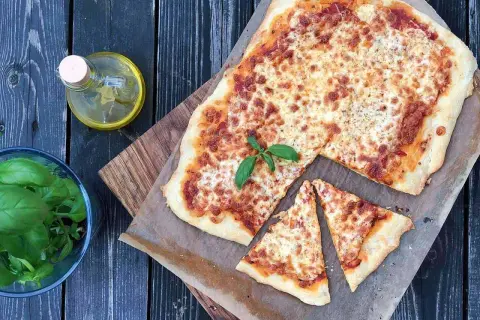 Pyszna pizza margherita z roztopionym serem i świeżą bazylią, obok butelka oliwy i miseczka ziół.