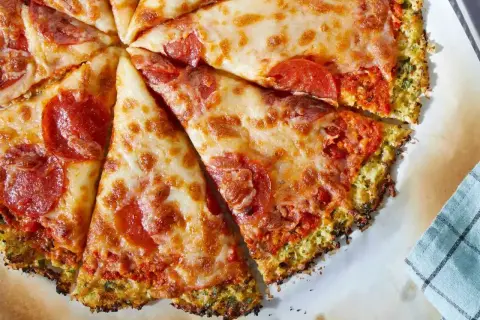 Pyszna pizza na spodzie z kalafiora z serem i pepperoni, pokrojona na kawałki.