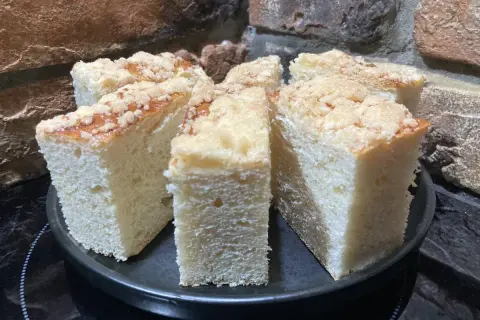 Puszyste ciasto drożdżowe z kruszonką, pokrojone na kawałki, prezentuje się apetycznie na czarnym talerzu.