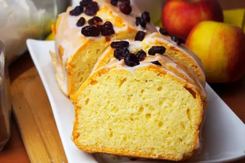 Najlepsza babka cytrynowa wilgotna na oleju, polana lukrem i posypana żurawiną. Obok jabłka.