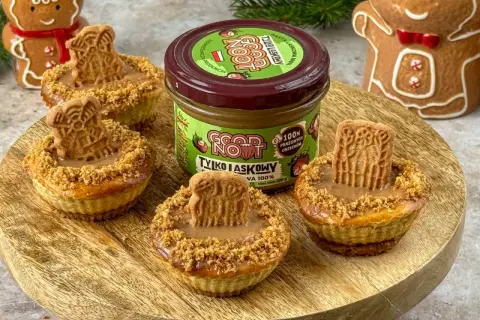 Urocze mini serniczki z kremem orzechowym i ciasteczkiem na wierzchu, obok słoiczek pasty z prażonych orzechów.