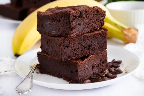 Stos puszystych brownie z bananami, ozdobiony ziarnami kawy, na talerzyku z łyżeczką.