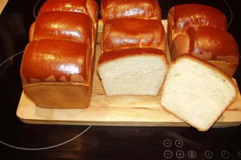 A fresh batch of chleb hokkaido, golden brown and fluffy, awaits. Two loaves are sliced, revealing their soft, airy crumb.
