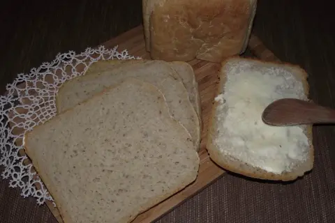 Chleb na zakwasie z maszyny, pokrojony w kromki, jedna posmarowana masłem.