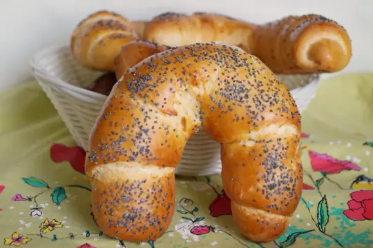 Złocisty rogal z makiem, świeżo upieczony, kusi swoim aromatem. W koszyku czekają kolejne pyszności.